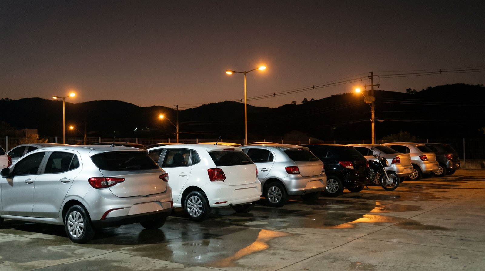 Pátio de seminovos ao anoitecer, iluminado por lâmpadas de luz quente.